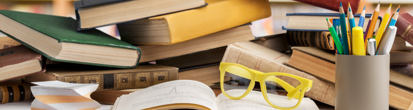 Rebecca Hughes | Exam Preparation – IELTS / FCE / TOEFL Banner Image | Messy desk with book piles and an open book with glasses on it. Pencil holder on the right